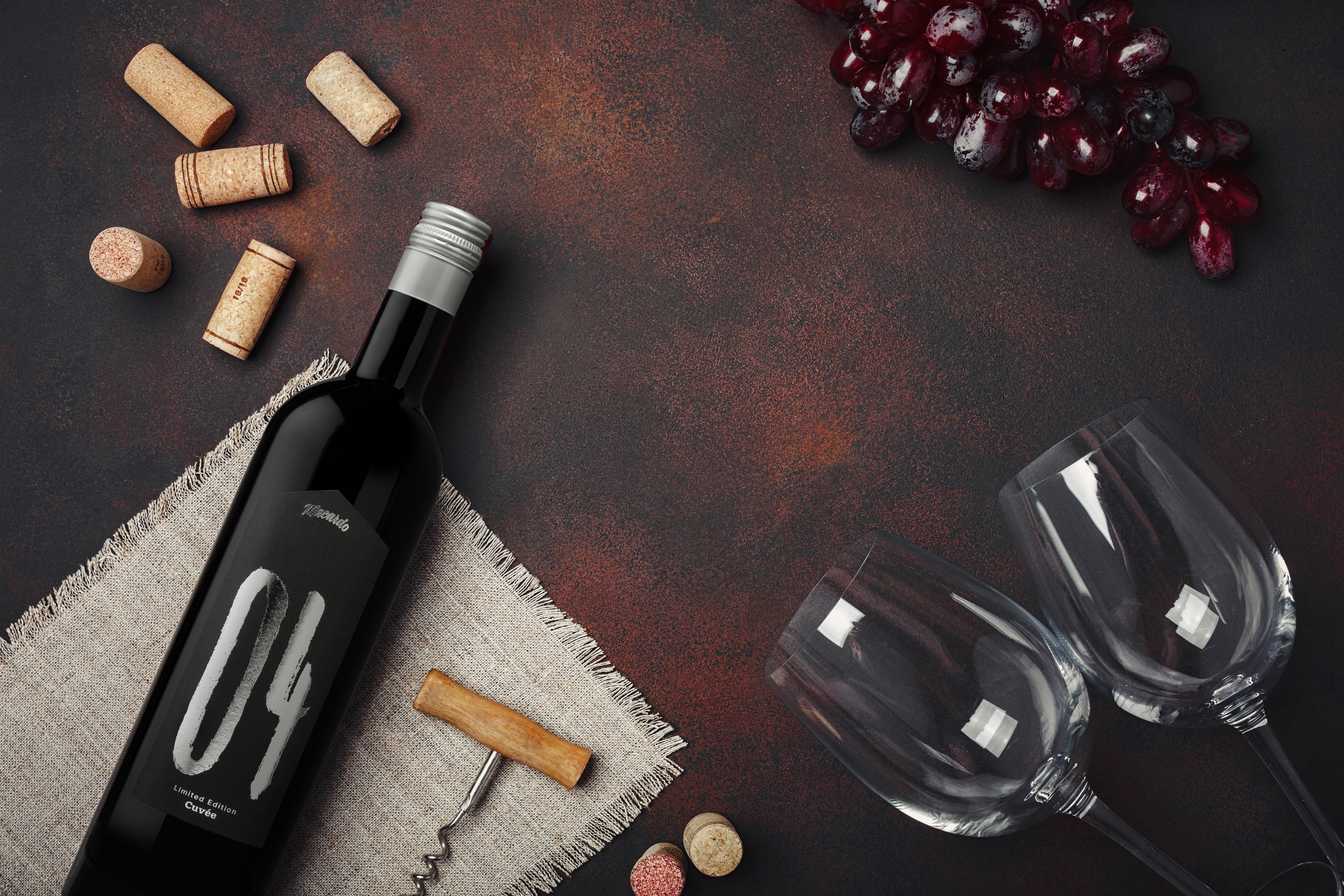 Dunkle Szene mit einer Flasche Rotwein "04" Cuvée, flankiert von Korken, einem Korkenzieher und einer Stoffserviette links. Rechts liegen leere Weingläser und eine Traube. Der Hintergrund ist dunkel und rustikal gehalten.